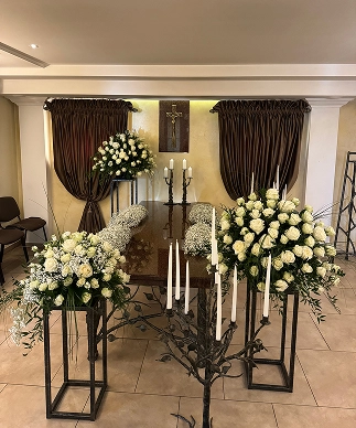 Šarvojimo salė su baltomis gėlėmis ir uždegtomis žvakėmis.