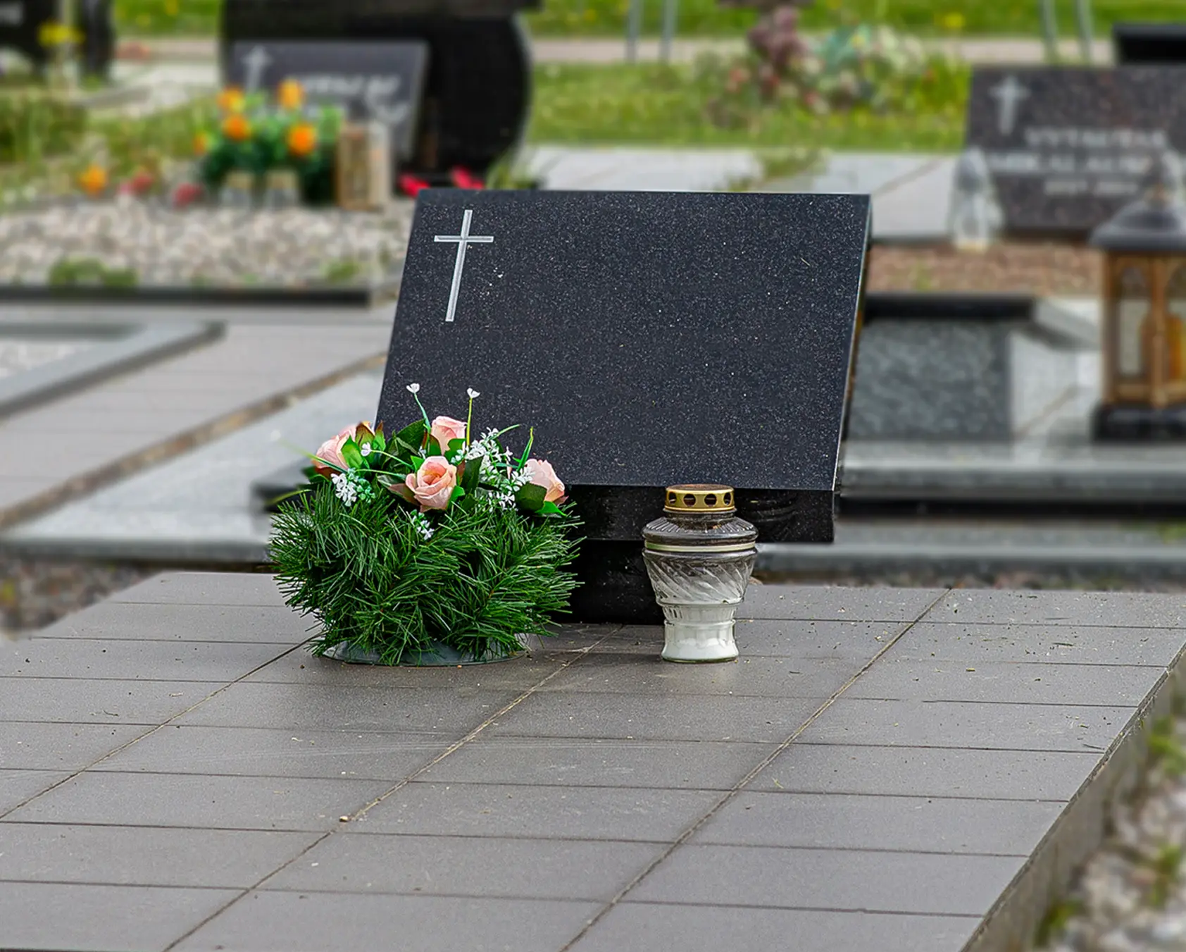 Plati juodo granito kapavietė su keliais paminklais ir tamsia dekoratyvine danga