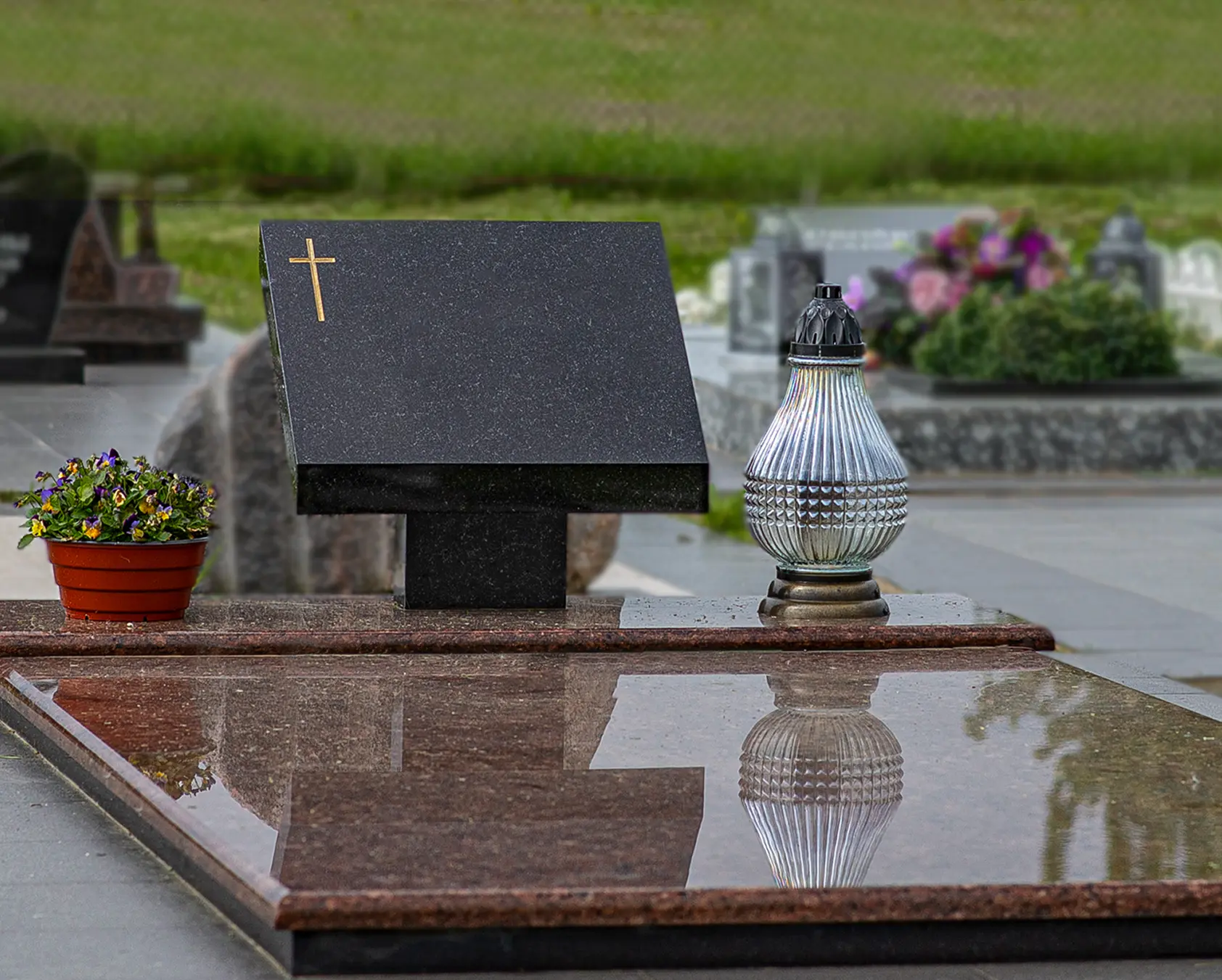 Plati juodo granito kapavietė su keliais paminklais ir tamsia dekoratyvine danga