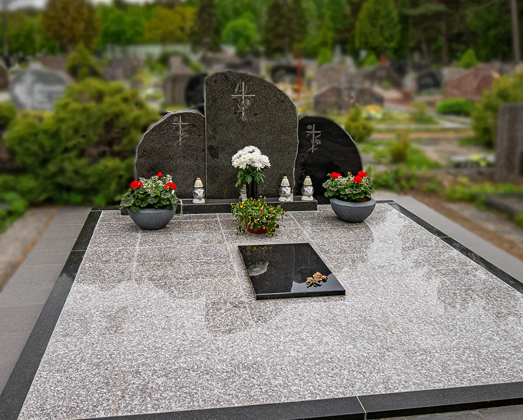 Plati juodo granito kapavietė su keliais paminklais ir tamsia dekoratyvine danga