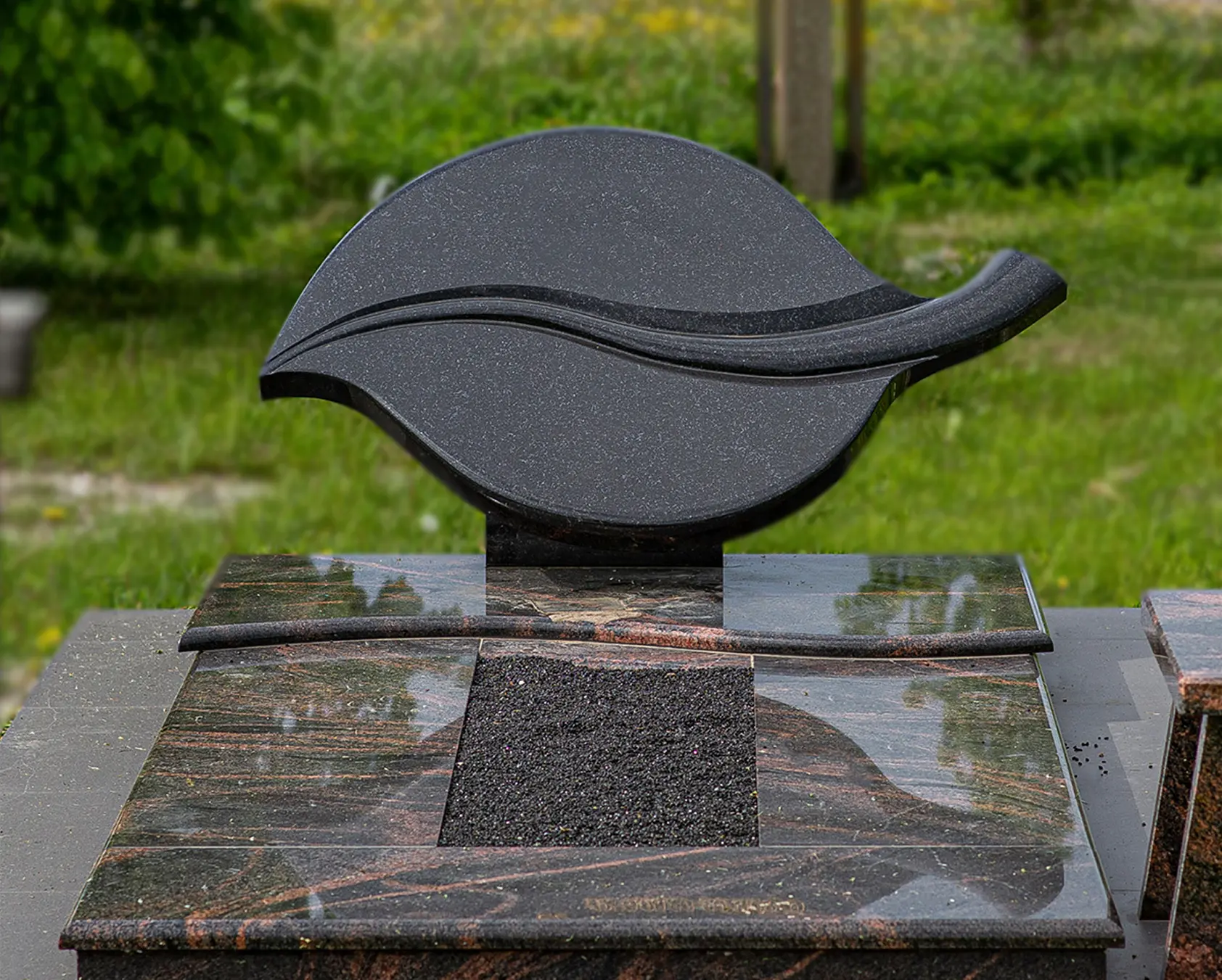 Plati juodo granito kapavietė su keliais paminklais ir tamsia dekoratyvine danga