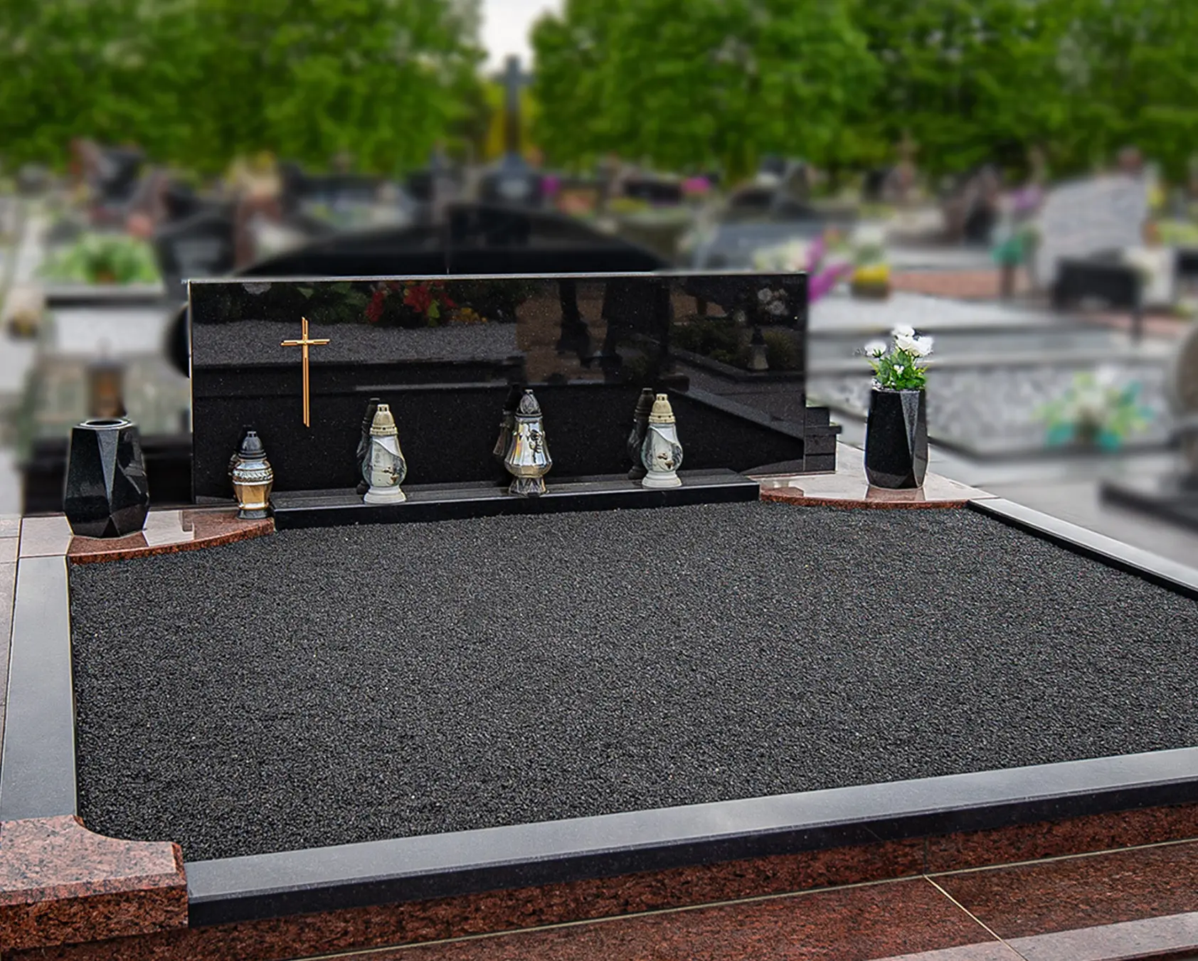 Plati juodo granito kapavietė su keliais paminklais ir tamsia dekoratyvine danga